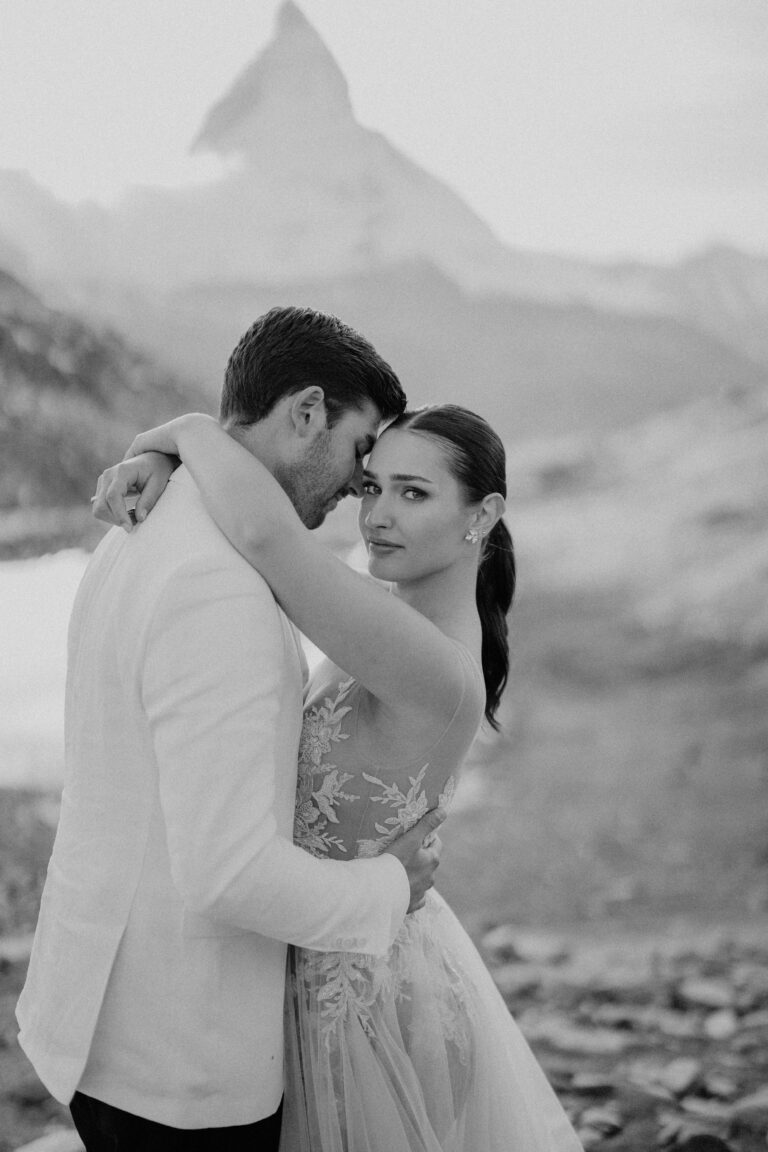 Ein Paar umarmt sich im Freien mit den Bergen im Hintergrund; die Frau schaut in die Kamera und fängt den perfekten Moment für einen italienischen Hochzeitsplaner ein.
