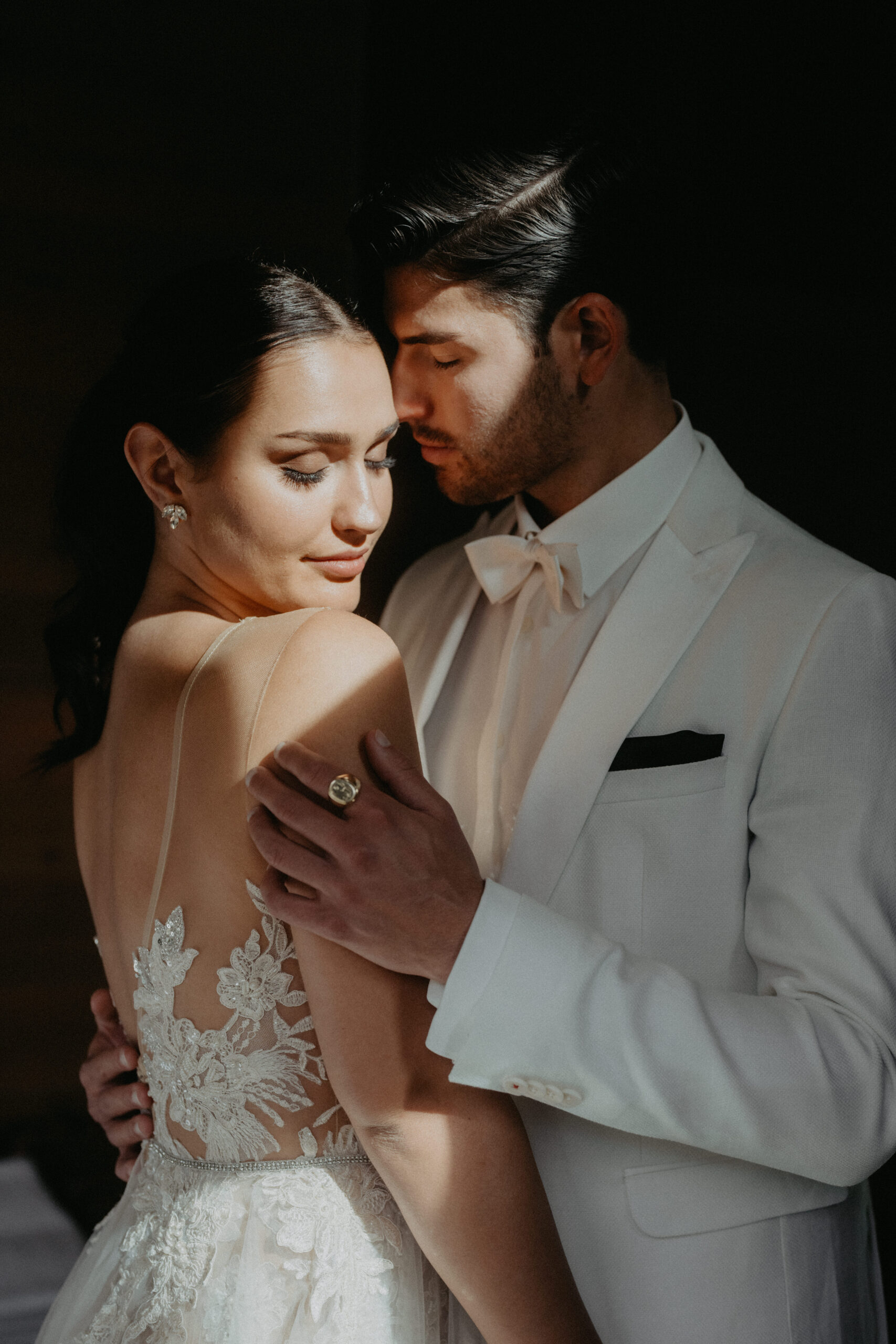 Eine Braut und ein Bräutigam in eleganter Hochzeitskleidung umarmen sich zärtlich in weichem, natürlichem Licht und fangen einen Moment ein, der von einem Wedding Planner in Italien oder der Schweiz perfekt geplant wurde.
