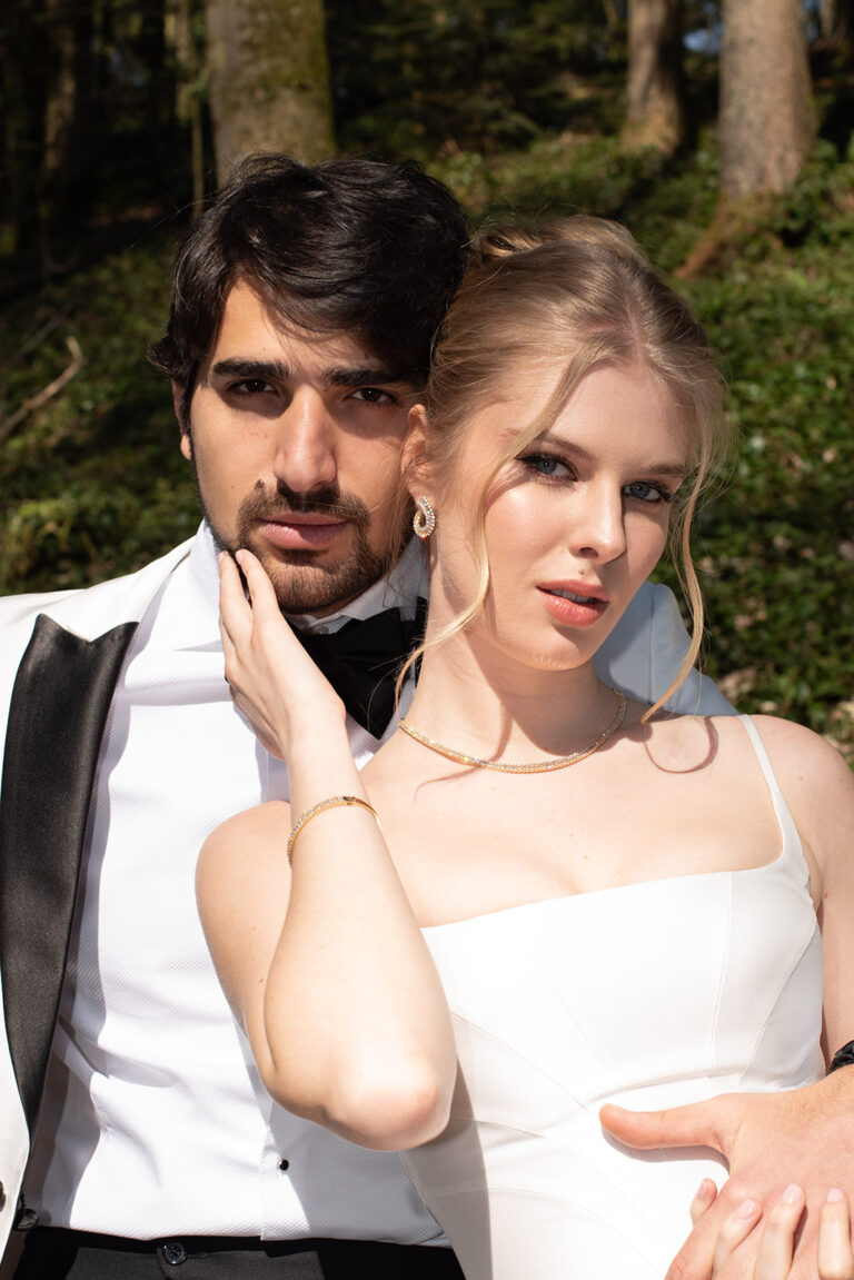 Ein formell gekleidetes Paar posiert eng beieinander im Freien und schaut selbstbewusst in die Kamera - ein idealer Moment für einen Wedding Planner, der Liebesgeschichten in der Schweiz oder in Italien festhält.