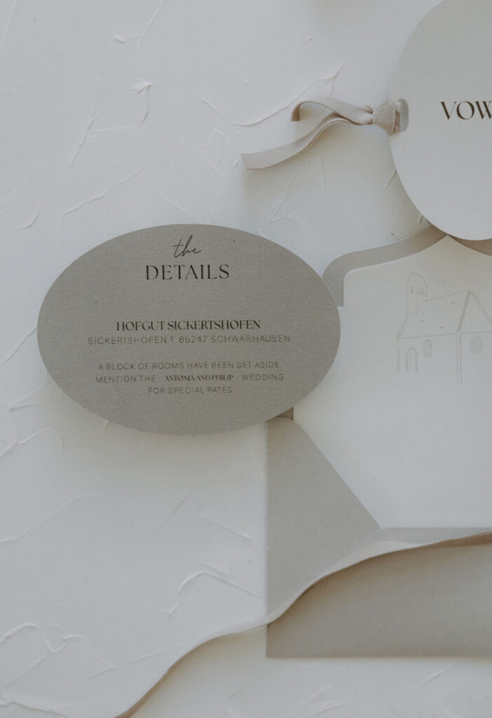 Ovale Hochzeitskarte mit minimalistischem grauen Text und Band auf strukturiertem weißen Hintergrund - perfekt für die Hochzeitsplanung in der Schweiz oder Italien.