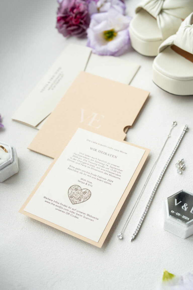 Hochzeitseinladung mit Schmuck, weißen Schuhen, lila Blumen und einer Ringschachtel auf einer weißen Fläche - die perfekte Inspiration für jeden Hochzeitsplaner, der eine romantische Feier in Italien plant.
