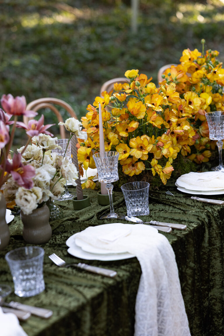Elegantes Tischset für den Außenbereich mit Kristallgläsern, weißen Tellern und leuchtend gelben und rosafarbenen Blumen - perfekt für die Hochzeitsplanung in Italien oder der Schweiz.