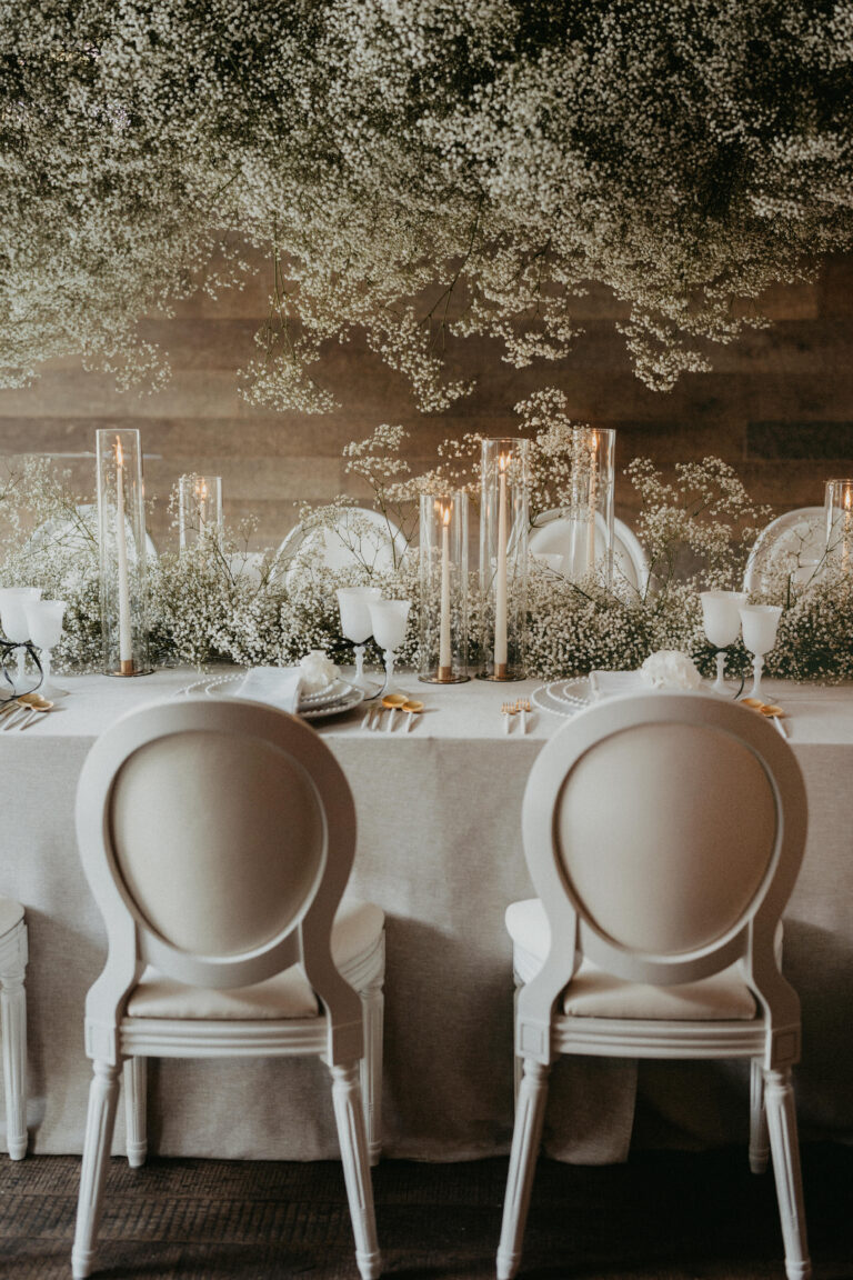 Elegante Tischdekoration mit weißen Stühlen, Kerzen und Babyatem-Blumen, die über und entlang des Tisches angeordnet sind - die perfekte Inspiration für Hochzeitsplaner in der Schweiz oder Italien.