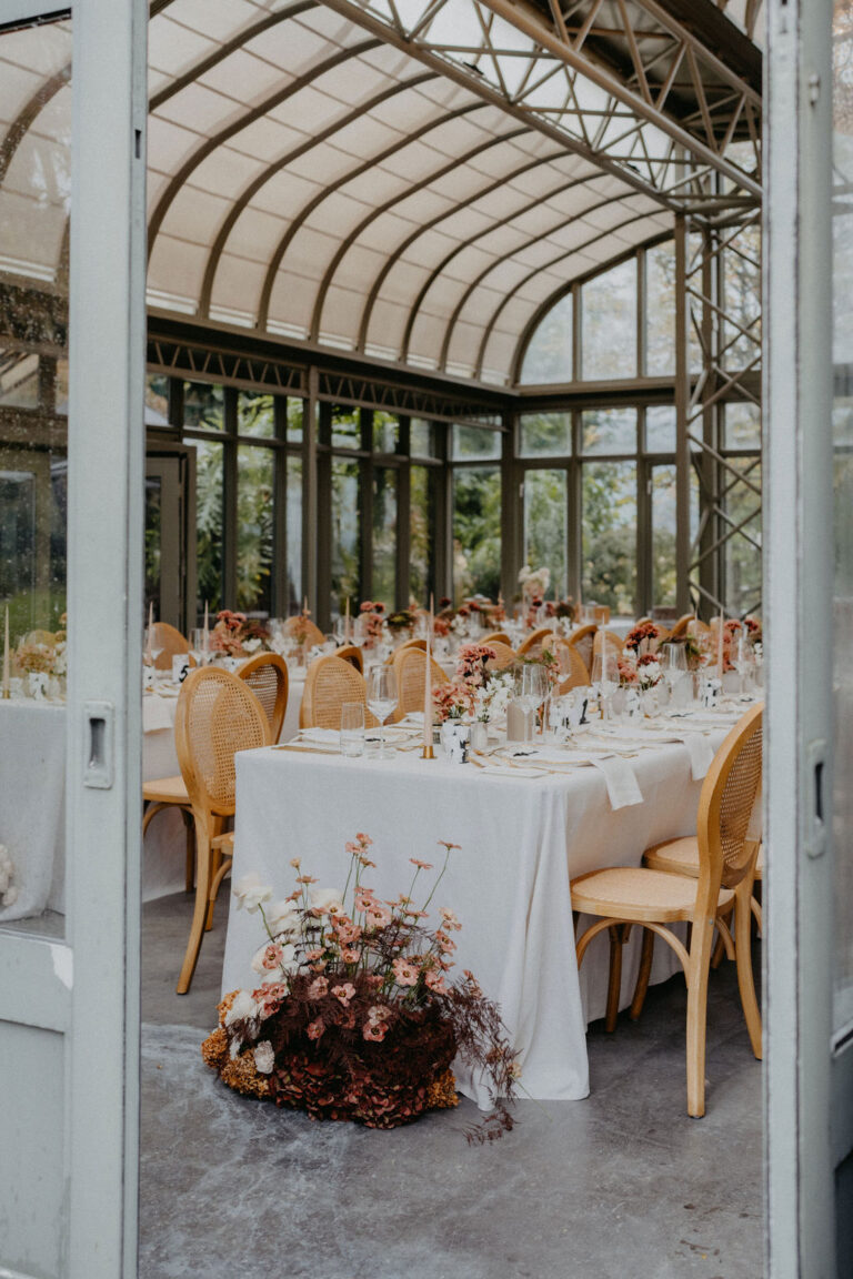 Elegante Esstische mit Blumenarrangements in einem gläsernen Wintergarten mit natürlichem Licht - die perfekte Inspiration für die Hochzeitsplanung in der Schweiz, geführt von einem erfahrenen Hochzeitsplaner.