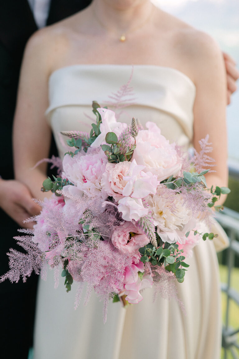 Frau in einem cremefarbenen Kleid mit einem Strauß rosa und weißer Blumen mit Grünzeug, perfekte Inspiration für jeden Hochzeitsplaner in der Schweiz oder Italien.