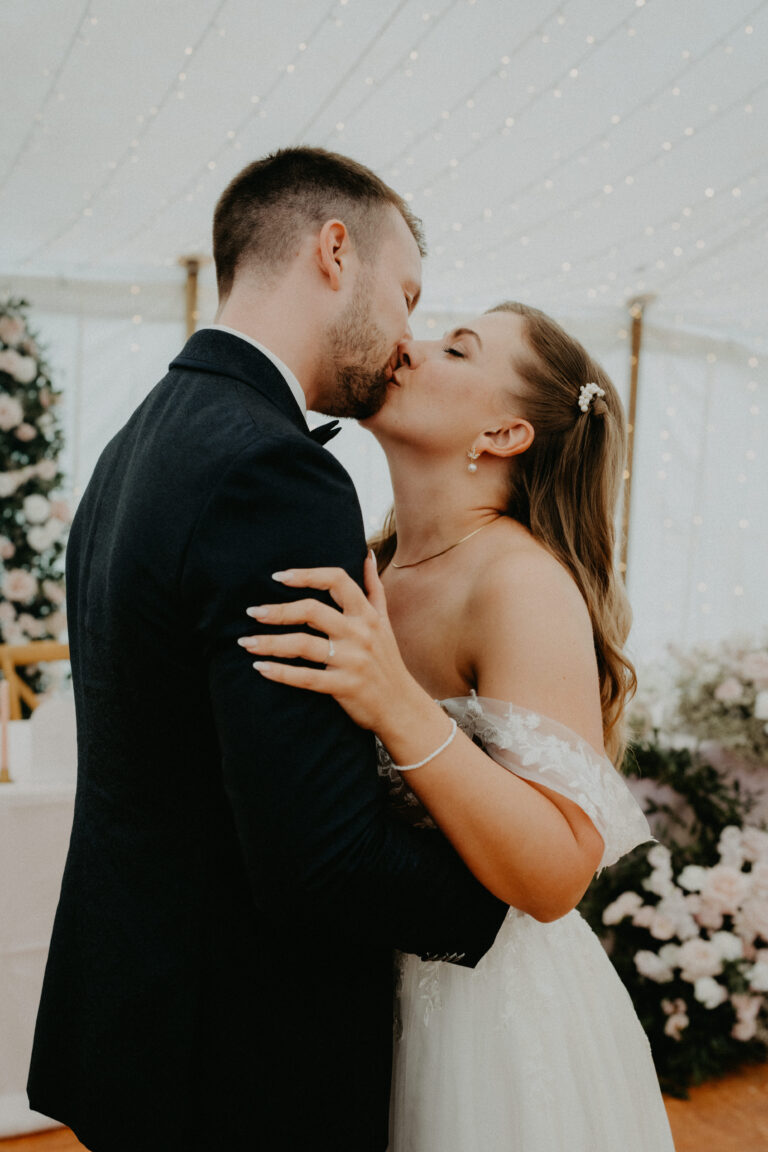 Braut und Bräutigam küssen sich bei ihrer Hochzeit in der Schweiz, umgeben von Blumen und sanften, funkelnden Lichtern - ein unvergesslicher Moment, der mit Hilfe eines Hochzeitsplaners geschaffen wurde.