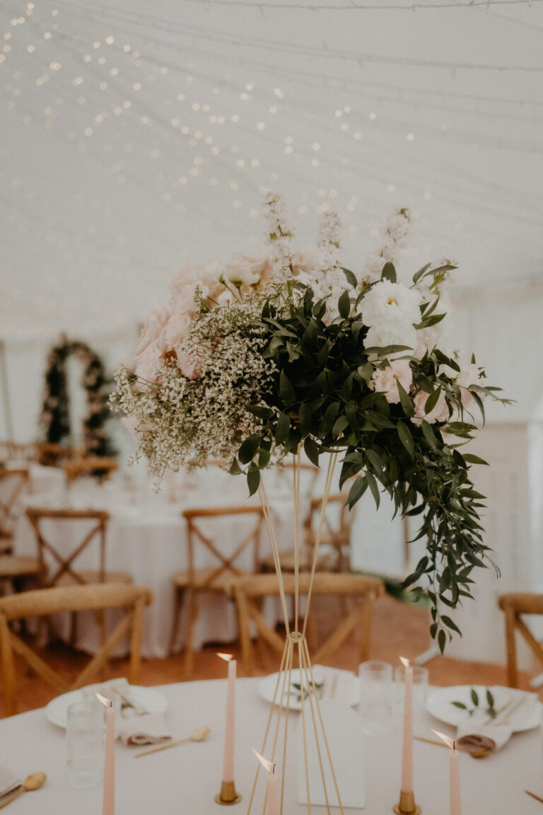 Großer Blumenschmuck auf einem runden Hochzeitstisch mit Kerzen, unter Lichterketten in einem wunderschön dekorierten Veranstaltungsort - die perfekte Inspiration für Ihre italienische Hochzeitsplanung oder die Vision eines Hochzeitsplaners.