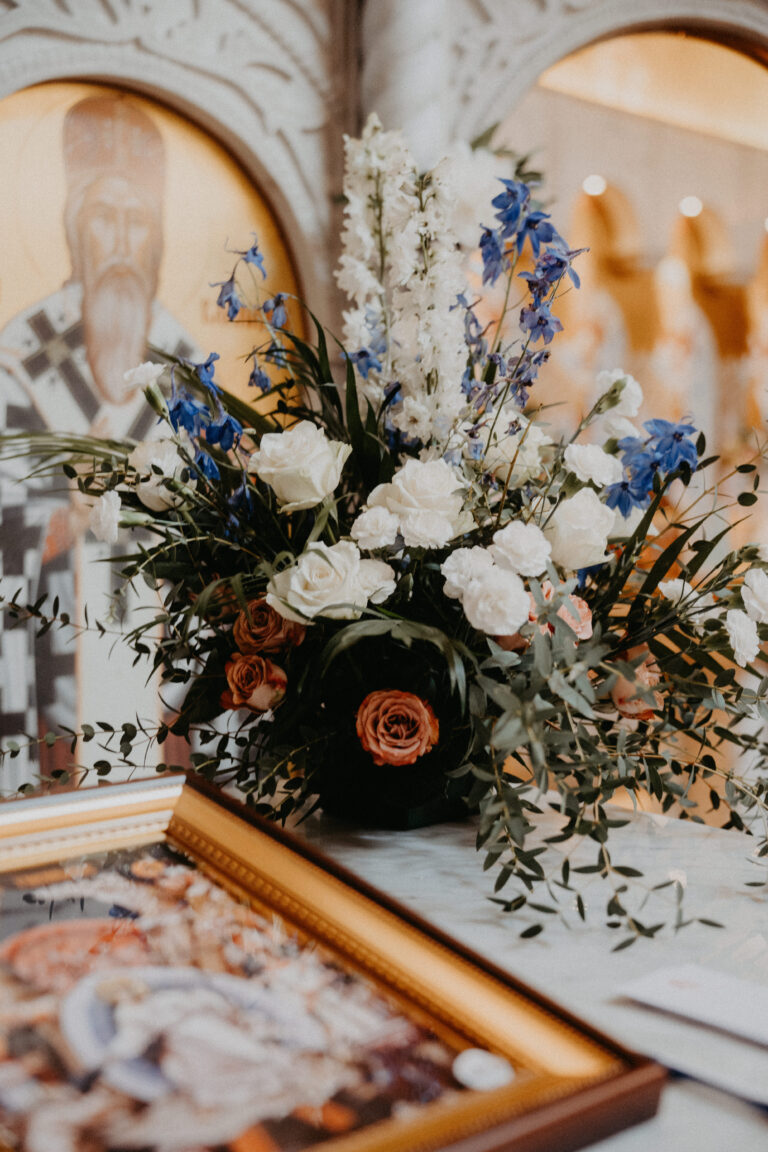 Ein Strauß weißer und blauer Blumen liegt auf einem Tisch neben einem gerahmten Foto in einer Kirche, arrangiert mit der Eleganz eines Hochzeitsplaners aus Italien oder der Schweiz.
