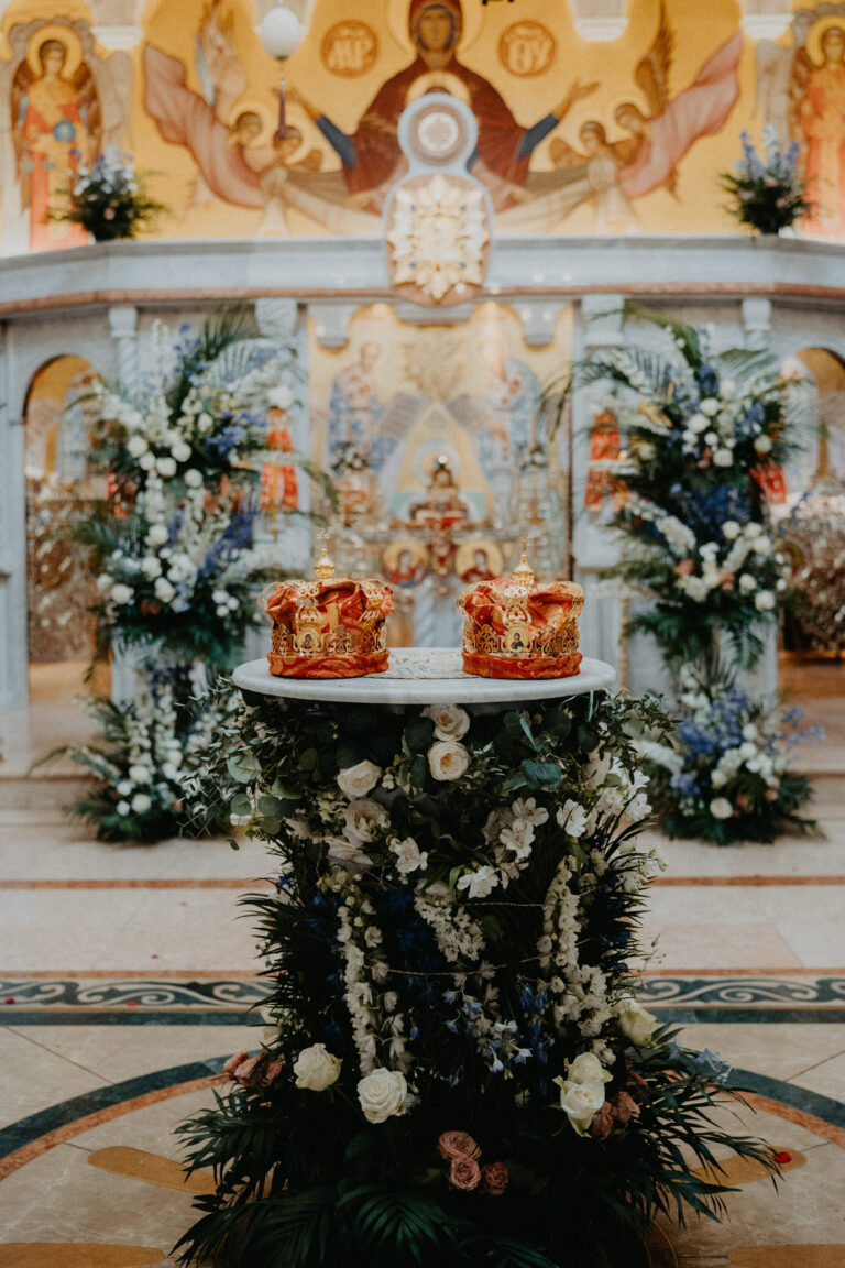 Zwei verschnörkelte Kronen ruhen auf einem blumengeschmückten Ständer in einer reich verzierten Kirche mit religiösen Ikonen - eine zeitlose Szene für jeden Hochzeitsplaner in Italien oder der Schweiz.