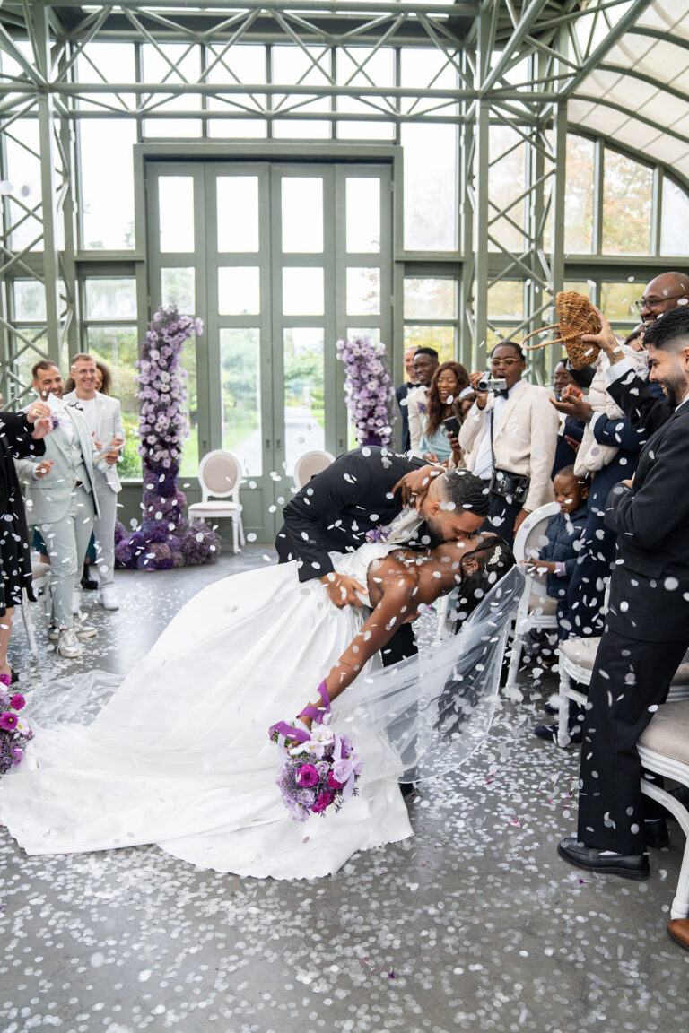 Braut und Bräutigam küssen sich, während die Gäste bei ihrer Indoor-Hochzeit Konfetti werfen, perfekt koordiniert von einem Hochzeitsplaner in der Schweiz.