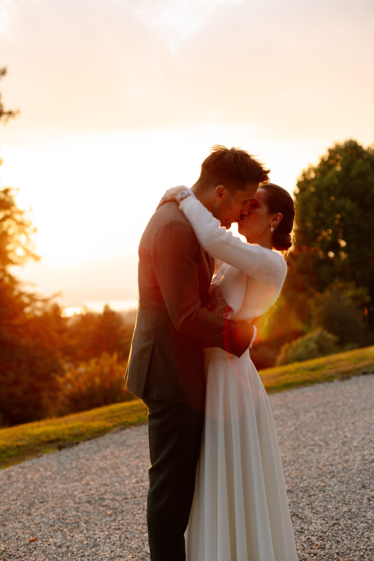 Braut und Bräutigam umarmen sich bei Sonnenuntergang unter freiem Himmel, getaucht in warmes, goldenes Licht - ein perfekter Moment, eingefangen durch professionelle Hochzeitsplanung.