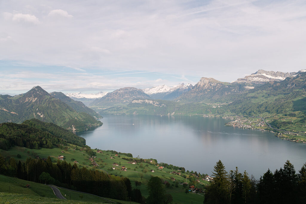 Ein ruhiger See, Vierwaldstättersee, umgeben von grünen Hügeln, verstreuten Häusern und schneebedeckten Bergen unter einem wolkenverhangenen Himmel - die perfekte Inspiration für jeden Hochzeitsplaner, der eine atemberaubende Hochzeitslocation sucht. Dies ist aus der Sicht von der Villa Honegg.