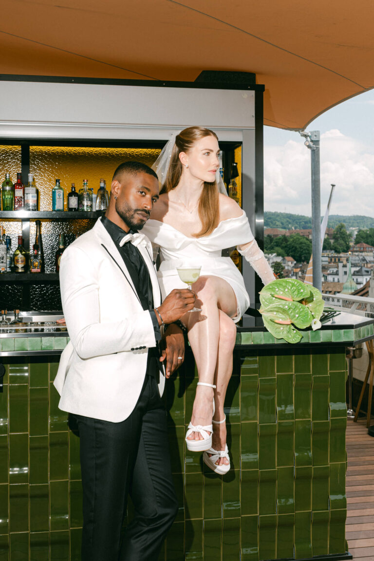 Braut und Bräutigam posieren in eleganter Hochzeitskleidung an einer Bar im Freien und halten Drinks in der Hand - ein unvergesslicher Moment, der von ihrem Hochzeitsplaner im Herzen der Schweiz festgehalten wurde.