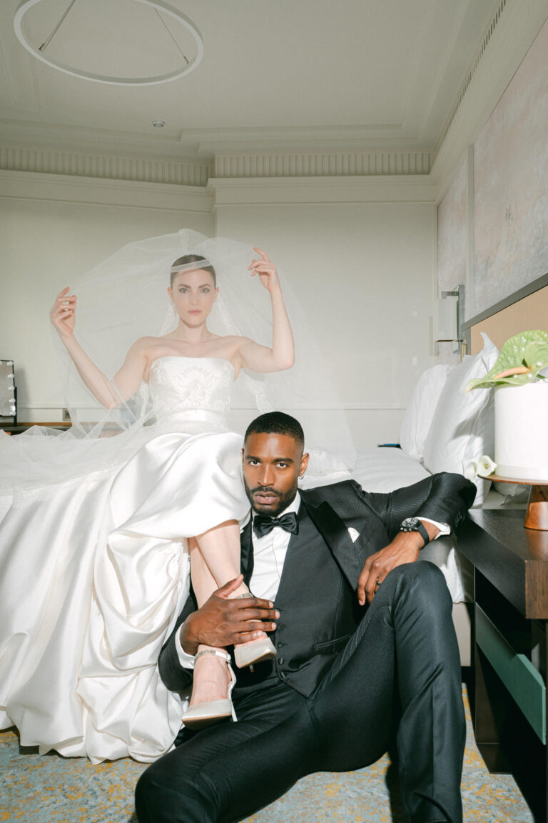 Eine Braut in einem weißen Kleid sitzt auf einem Bett, während der Bräutigam im Smoking auf dem Boden sitzt und ernst dreinschaut - vielleicht denken sie über ihre Hochzeitsplanung für eine Traumhochzeit in Italien nach.