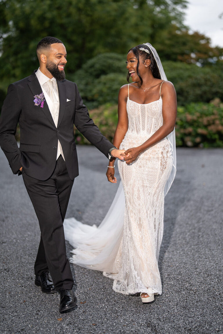 Eine lächelnde Braut und ein lächelnder Bräutigam gehen Hand in Hand in eleganter Hochzeitskleidung nach draußen, ihre Freude wird von einem talentierten Wedding Planner in der malerischen Schweiz eingefangen.