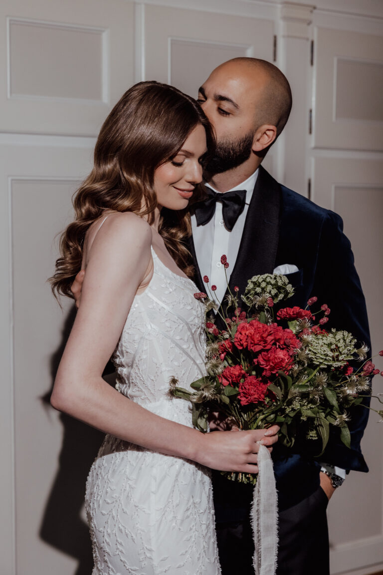 Ein Mann im Anzug küsst eine Frau im weißen Kleid, die einen Blumenstrauß hält. Ein romantischer Moment, perfekt für jeden Hochzeitsplaner in der Schweiz oder in Italien.