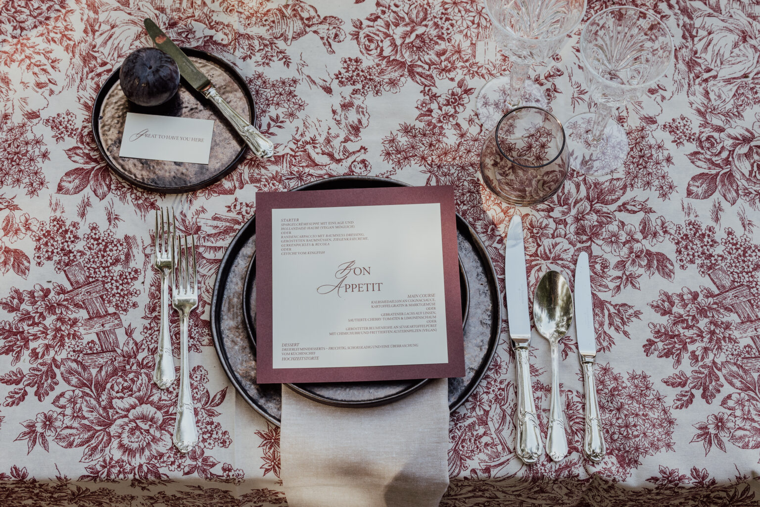 Home 11 Eleganter, blumengeschmückter Tisch mit Menüs, Tellern, Besteck und Gläsern, ordentlich auf einer gemusterten Tischdecke arrangiert - die perfekte Inspiration für die Hochzeitsplanung in der Schweiz oder die Beratung durch einen erfahrenen Wedding Planner.