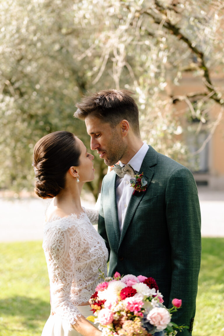 Braut und Bräutigam in Hochzeitskleidung schauen sich im Freien liebevoll an und halten einen bunten Blumenstrauß in der Hand - ein perfekter Moment, der von ihrem Wedding Planner bei der professionellen Hochzeitsplanung eingefangen wurde.