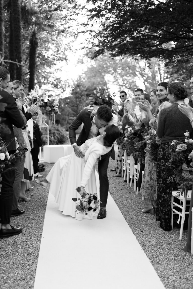 Ein Paar küsst sich bei seiner Hochzeit in der Schweiz, umgeben von jubelnden Gästen auf einem Gang im Freien dank nahtloser Hochzeitsplanung.