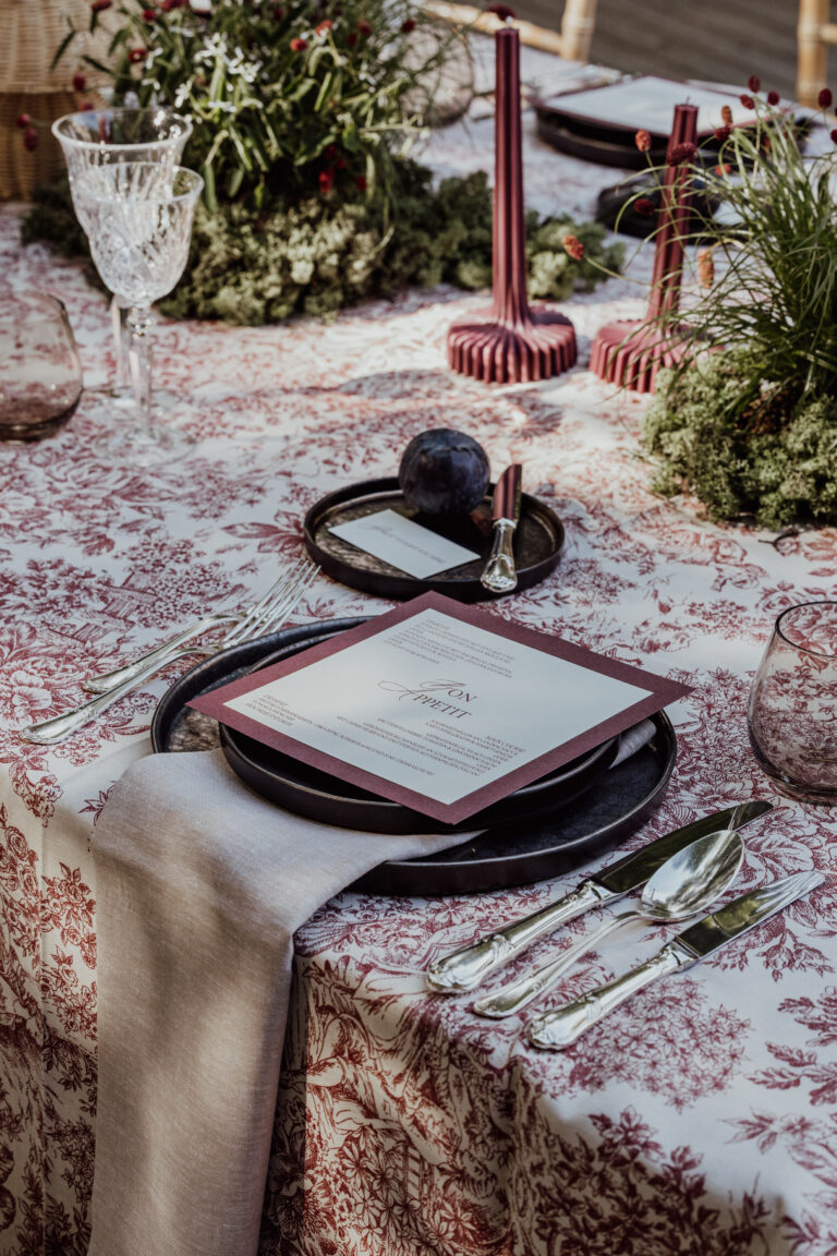 Eleganter gedeckter Tisch mit Blumentischdecke, Menükarte, Silberbesteck, Kristallglas und weinroten Kerzen - die perfekte Inspiration für jeden Hochzeitsplaner in der Schweiz.