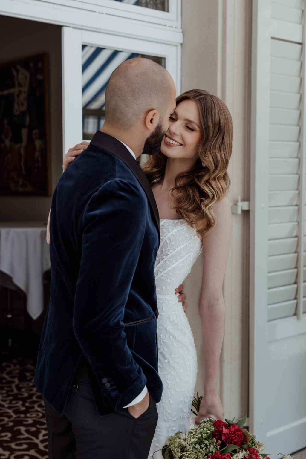 Home 6 Eine Braut und ein Bräutigam umarmen sich und lächeln sich an einer Tür mit einem Blumenstrauß in der Hand an und fangen den Zauber ein, der von einem erfahrenen Hochzeitsplaner in Italien geschaffen wurde.