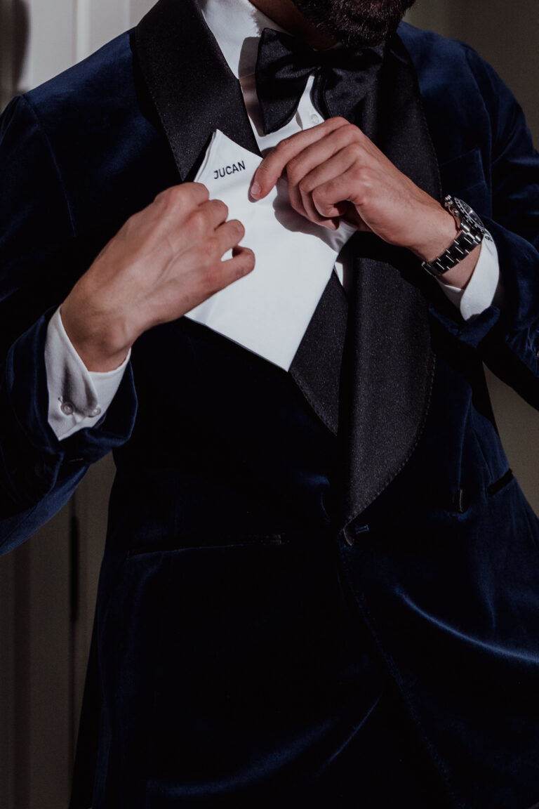 Ein Mann im dunklen Samt-Smoking steckt inmitten einer eleganten Hochzeitsplanung einen Umschlag mit der Aufschrift JUCAN in seine Jackentasche - ein Hinweis auf den zeitlosen Charme Italiens und die Raffinesse der Schweiz.