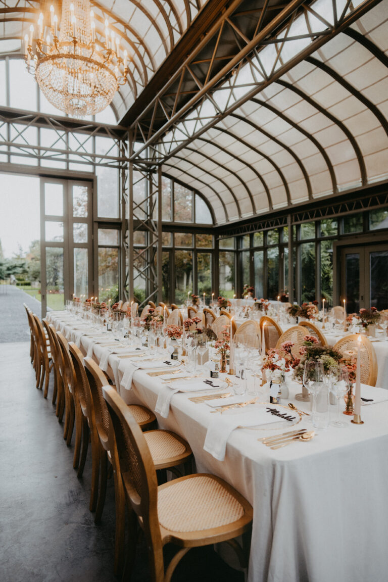 Eleganter, mit Blumen und Kerzen gedeckter Banketttisch in einem gläsernen, sonnendurchfluteten Veranstaltungsraum - perfekt für die Hochzeitsplanung in der Schweiz mit der Expertise eines engagierten Wedding Planners.