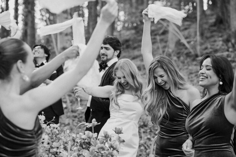 Menschen in förmlicher Kleidung feiern im Freien, lächeln und winken mit Servietten und Blumen im Vordergrund - perfekt für eine Traumhochzeit, die von einem Schweizer Wedding Planner geplant wurde oder vor der romantischen Kulisse Italiens.