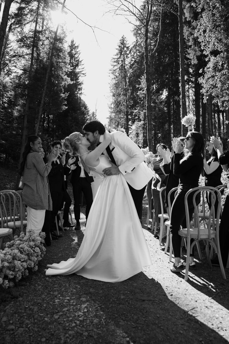 Braut und Bräutigam küssen sich im Freien in der Schweiz, während die Hochzeitsgäste um sie herum jubeln und applaudieren - ein magischer Moment der perfekten Hochzeitsplanung.