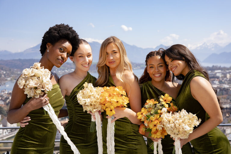 Fünf Frauen in grünen Kleidern, die Blumensträuße halten, lächelnd mit Blick auf die Berge und den See in der Schweiz - ein unvergesslicher Moment, eingefangen von einem talentierten Hochzeitsplaner.