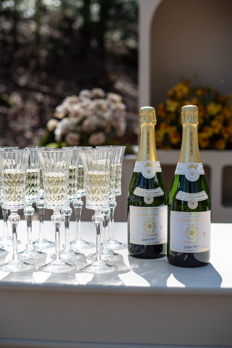 Zwei Flaschen Champagner und mehrere gefüllte Gläser auf einem Tisch mit Blumen im Hintergrund - perfekt für eine Hochzeitsfeier, die von einem professionellen Wedding Planner in der Schweiz geplant wird.