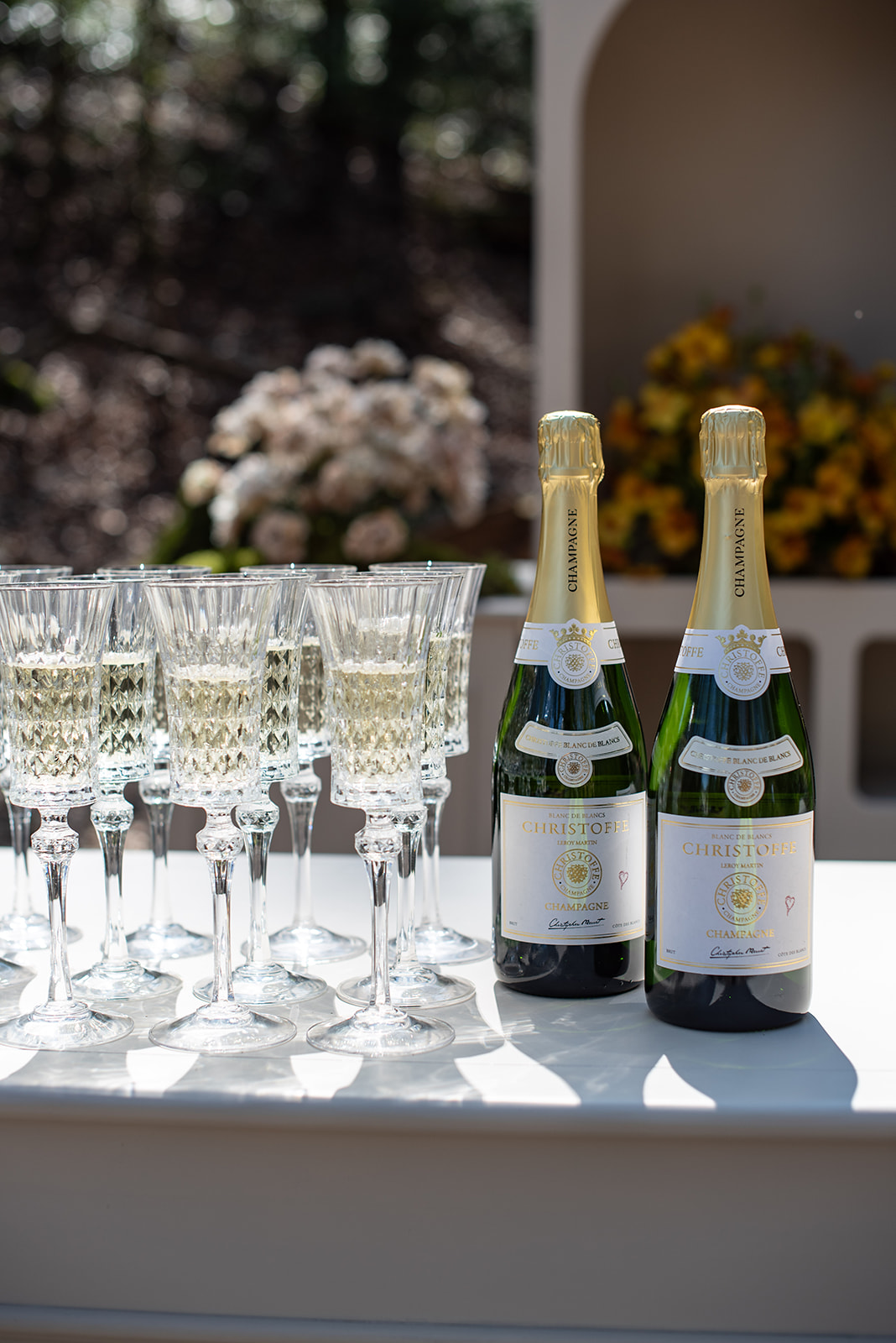 Zwei Flaschen Champagner und mehrere gefüllte Gläser auf einem Tisch mit Blumen im Hintergrund - perfekt für eine Hochzeitsfeier, die von einem professionellen Wedding Planner in der Schweiz geplant wird.