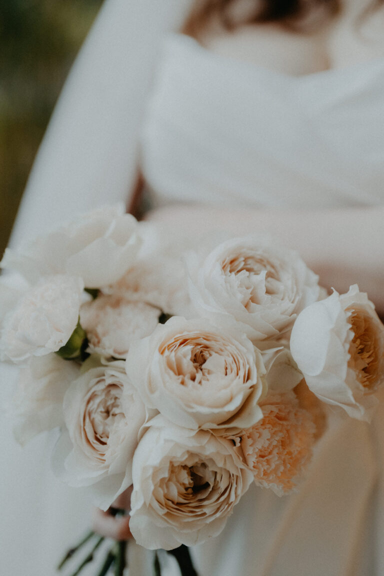 Eine Braut in Weiß mit einem Strauß aus cremefarbenen Rosen und Pfingstrosen, perfekt für eine romantische Hochzeit, geplant von einem Hochzeitsplaner in der Schweiz oder Italien.