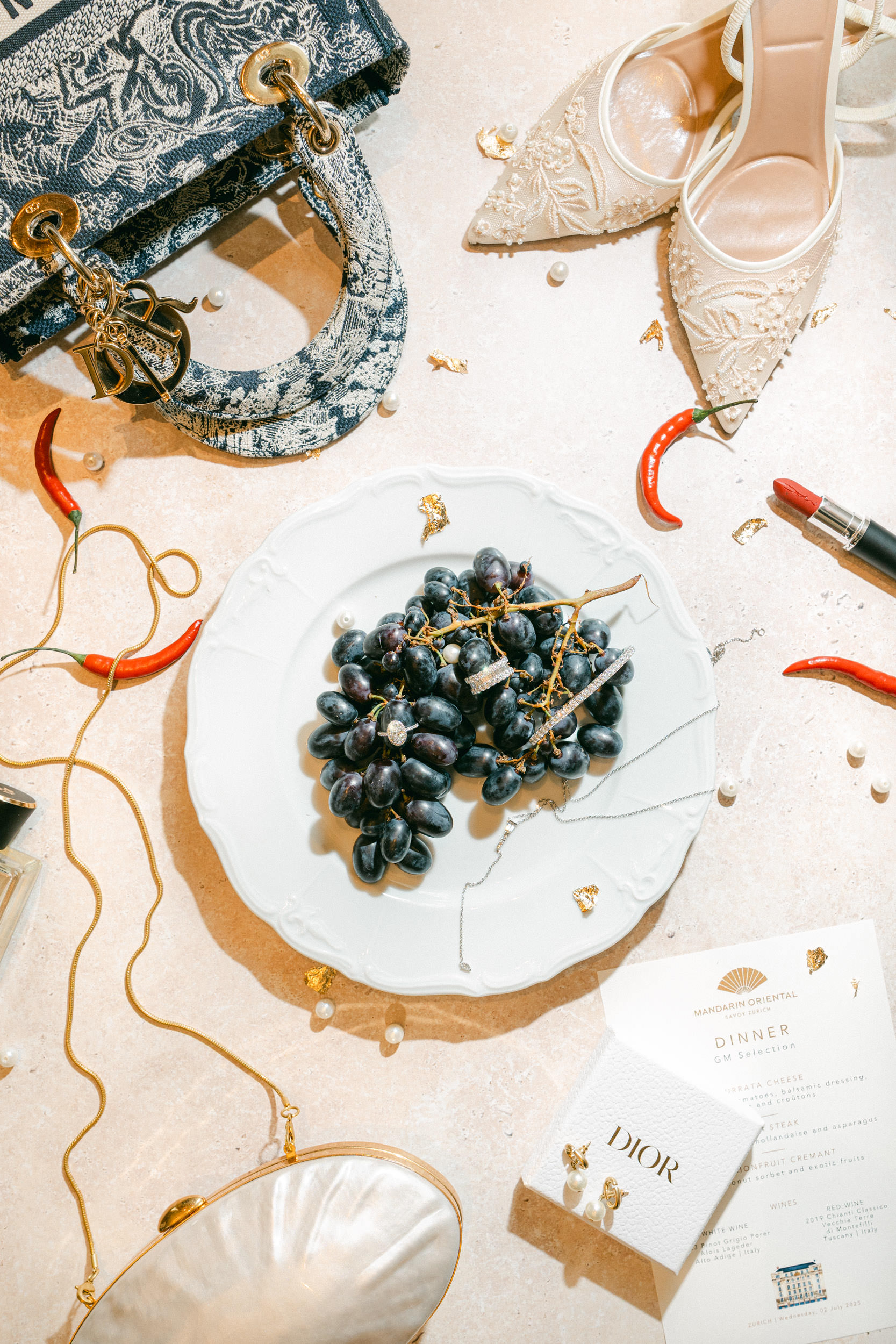 Ein Teller mit Weintrauben, umgeben von Luxus-Accessoires, roten Chilischoten, Lippenstift und hochhackigen Schuhen erinnert an den Glamour Italiens - die perfekte Inspiration für jeden Hochzeitsplaner in der Schweiz.