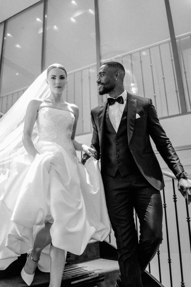 Eine Braut und ein Bräutigam gehen gemeinsam eine Treppe hinunter, beide sind förmlich gekleidet und sehen elegant aus - ein bezaubernder Moment, eingefangen von einem erfahrenen Wedding Planner im Herzen der Schweiz.