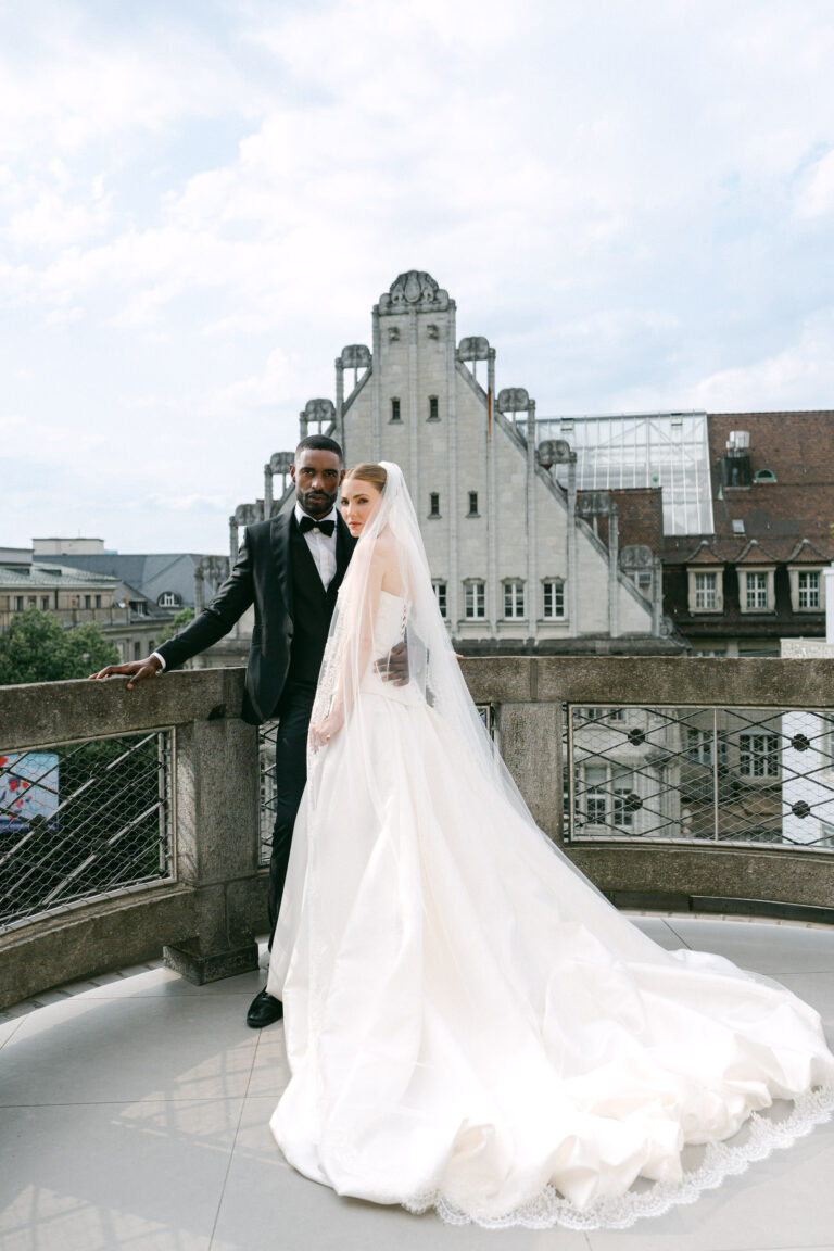 Braut im weißen Kleid und Bräutigam im Smoking stehen auf einem Balkon mit historischen Gebäuden im Hintergrund - ein unvergesslicher Moment, der durch professionelle Hochzeitsplanung in Italien perfekt gemacht wird.