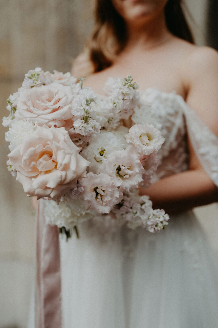 Die Braut im weissen Kleid hält einen Strauss aus zartrosa und weissen Blumen, perfekt für eine romantische Feier in der Schweiz oder in Italien, geplant von einem erfahrenen Wedding Planner.