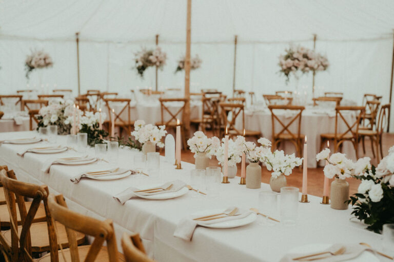 Eleganter Hochzeitsempfang in Italien mit langen Tischen, weißer Bettwäsche, Blumenschmuck und Holzstühlen in einem Zelt - perfekt gestylt von einem erfahrenen Wedding Planner.