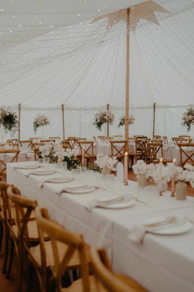 Eleganter Hochzeitsempfang mit langen Tischen, Blumenarrangements und Lichterketten unter einem weißen Zelt - perfekt für alle, die eine fachkundige Hochzeitsplanung in der Schweiz oder die Beratung durch einen professionellen Wedding Planner suchen.
