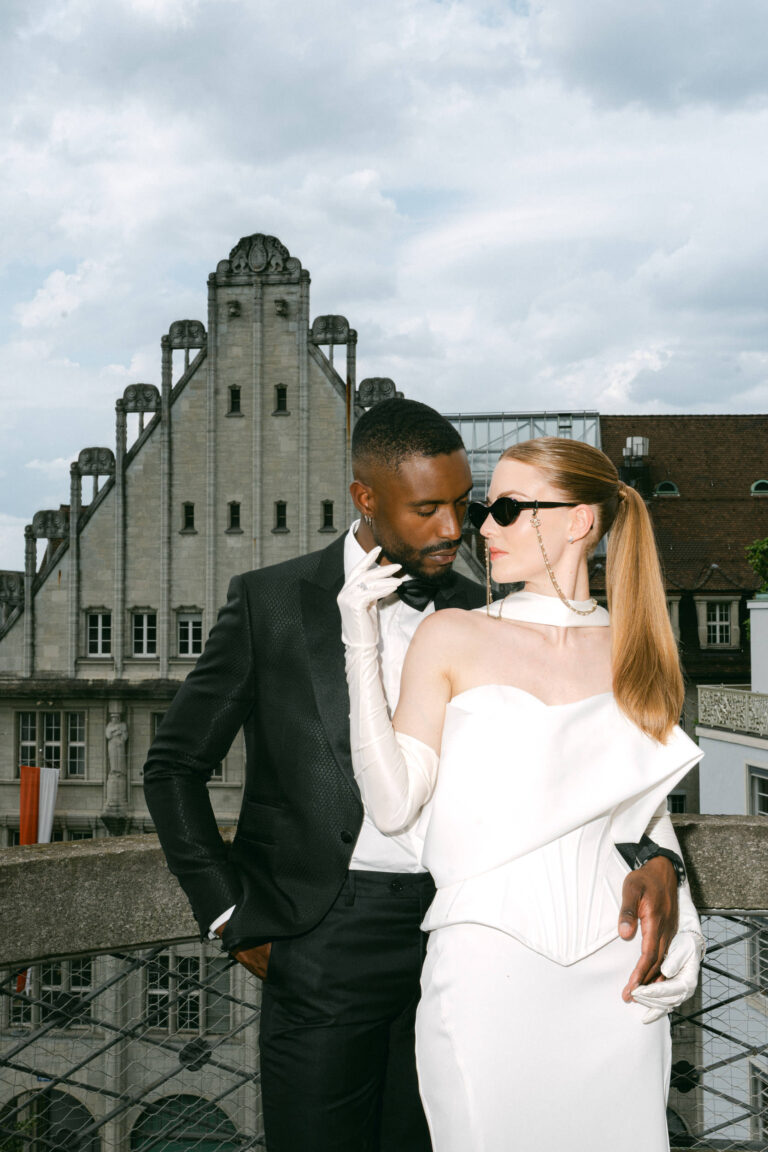 Ein stilvolles Paar in förmlicher Kleidung posiert auf einem Dach in Italien, mit einem historischen Gebäude im Hintergrund - die perfekte Inspiration für jeden Hochzeitsplaner oder Wedding Planner, der unvergessliche Momente sucht.