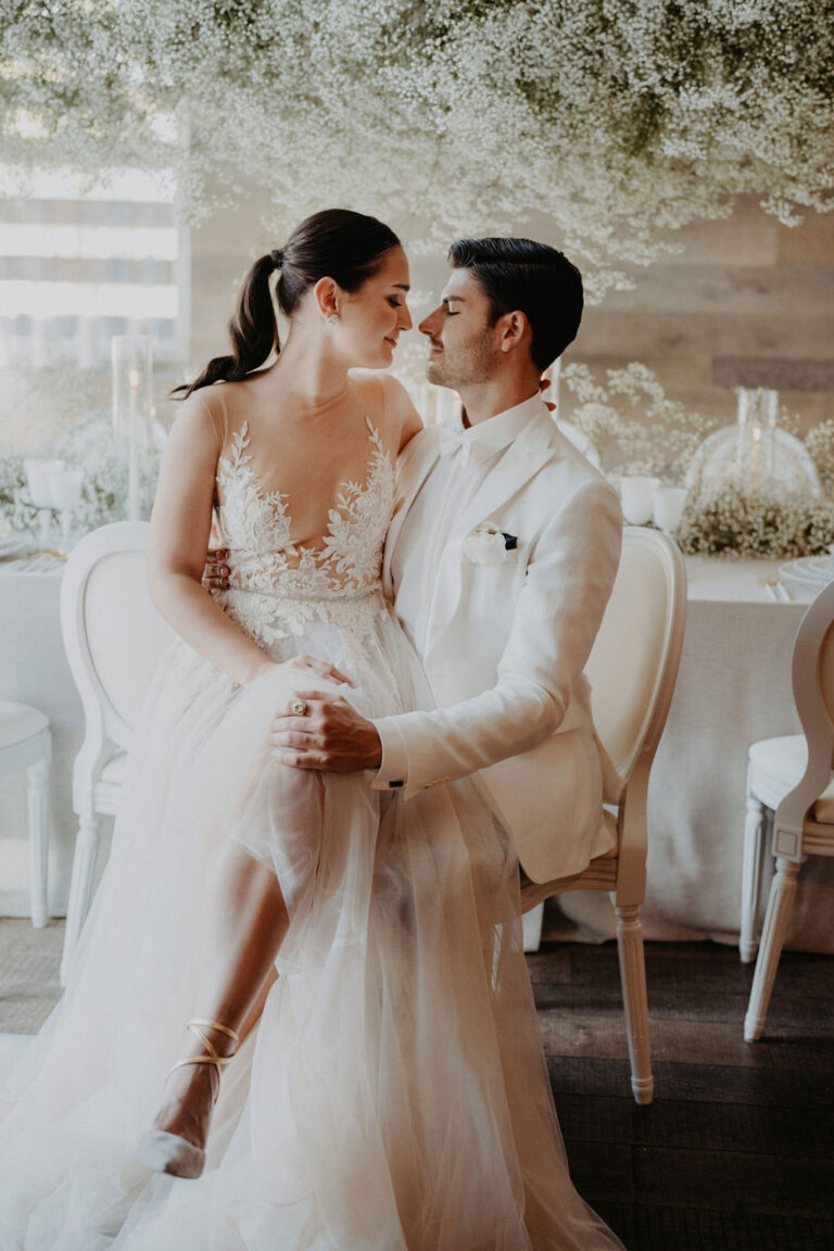 Braut und Bräutigam in eleganten weißen Kleidern sitzen eng beieinander und schauen sich liebevoll an bei ihrer Hochzeit in der Schweiz, eine Szene wie aus einem Hochzeitsplaner-Traum.
