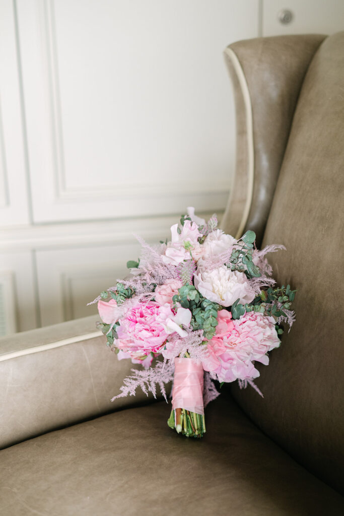 Auf einem taupefarbenen Ledersessel ruht ein Strauß aus rosa und weißen Blumen mit Grünzeug - die perfekte Inspiration für Ihre Hochzeitsplanung als Wedding Planner in der Schweiz. Hier in der Villa Honegg. 
