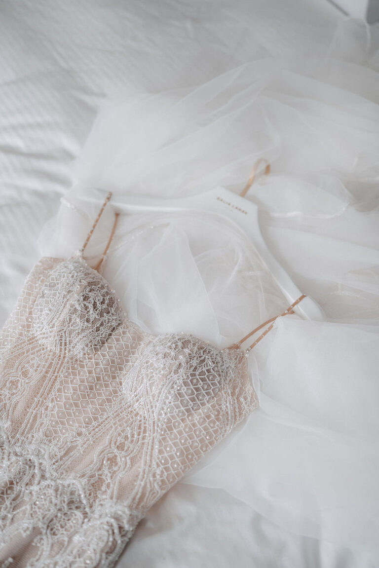 Hochzeitskleid und Schleier aus Spitze auf einem weißen Kleiderbügel, ausgelegt auf einem Bett - die perfekte Inspiration für jeden Wedding Planner in Italien.