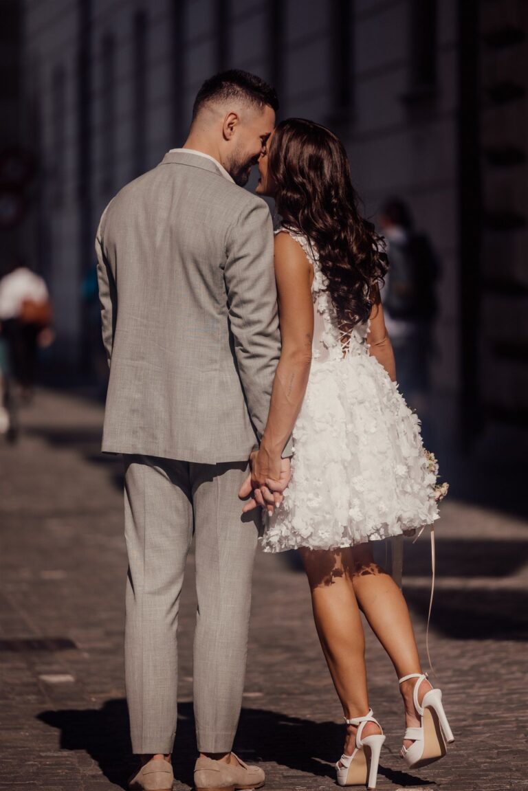 Ein Paar in Hochzeitskleidung hält sich an den Händen und küsst sich, während es eine sonnenbeschienene Straße entlangläuft. Ein perfekter Moment der Liebe und Freude - eine Inspiration für jeden Hochzeitsplaner oder Wedding Planner.