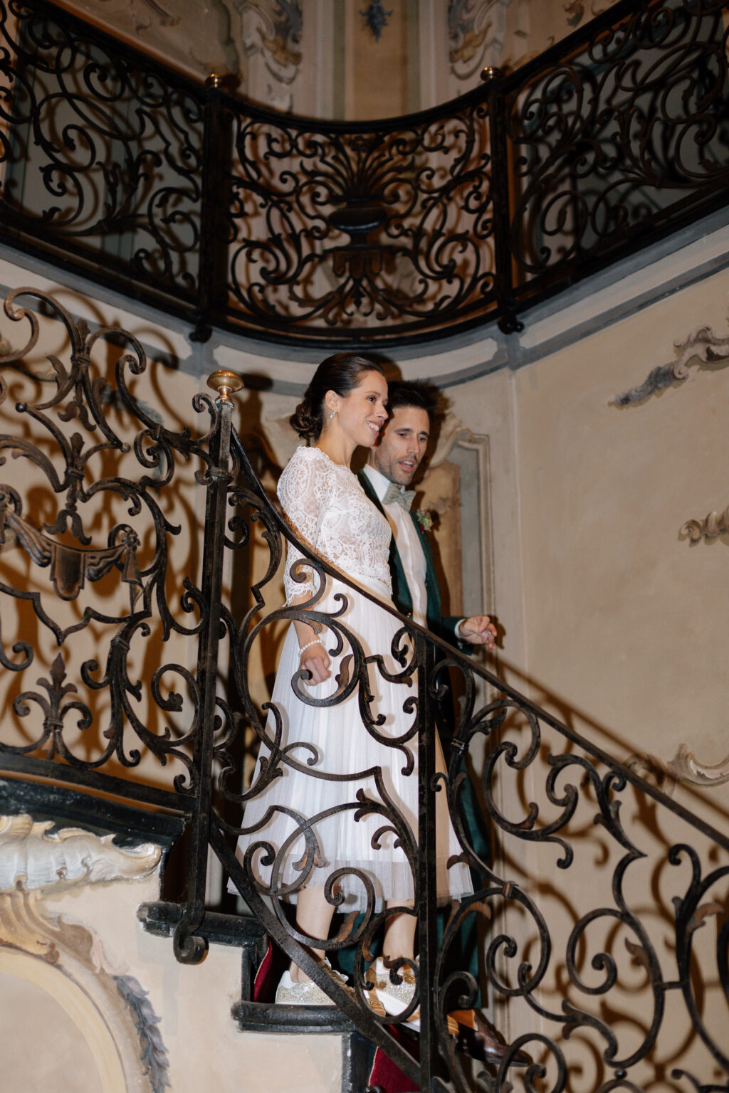 Home 29 Zwei Frauen in eleganten Kleidern steigen eine verschnörkelte, schmiedeeiserne Wendeltreppe in einem wunderschön dekorierten Innenraum hinunter - die perfekte Inspiration für jeden italienischen Hochzeitsplaner, der nach einzigartigen Ideen für die Hochzeitsplanung sucht.