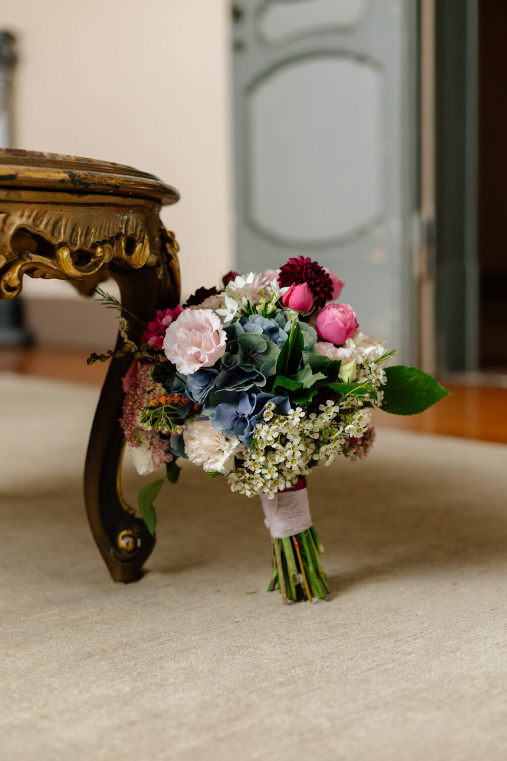 Home 19 Ein bunter Blumenstrauß liegt auf dem Boden neben einem verschnörkelten Holzstuhl - die perfekte Inspiration für jeden Hochzeitsplaner, der nach eleganten Ideen für die Hochzeitsplanung sucht.