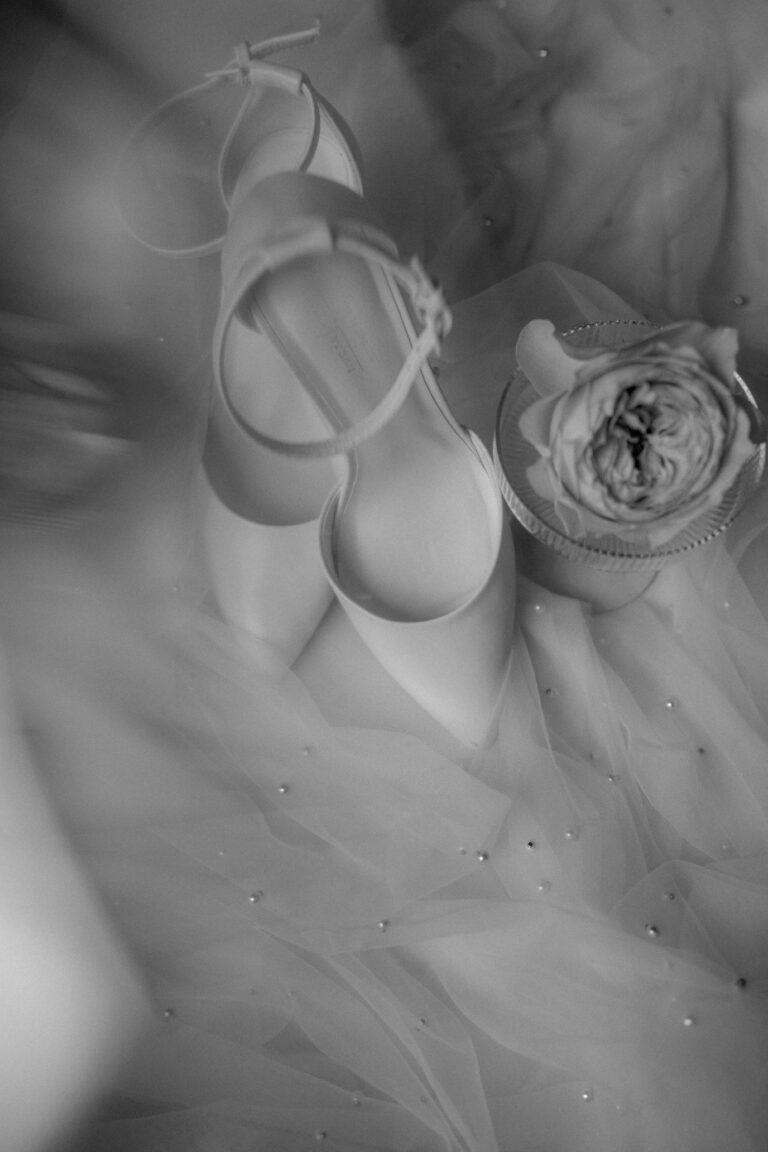 Weiße Ballerinas und eine Rose auf durchsichtigem Stoff mit kleinen Perlen, in sanfter schwarz-weißer Beleuchtung - die perfekte Inspiration für eine Hochzeitsplanerin in der Schweiz oder in Italien.