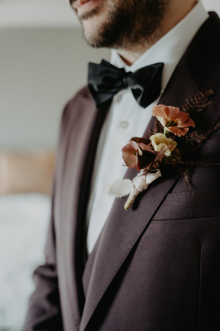 Mann im dunklen Anzug mit schwarzer Fliege und einer Blumenboutonniere am Revers, perfekt für eine elegante Hochzeit in der Schweiz oder eine romantische Hochzeit, die mit Ihrem Lieblings-Hochzeitsplaner in Italien geplant wurde.