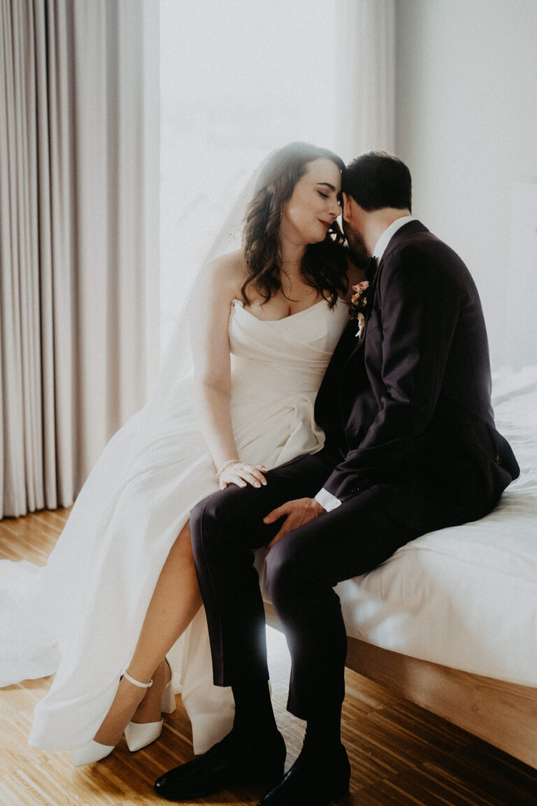 Braut und Bräutigam sitzen eng beieinander auf einem Bett und teilen einen intimen Moment an ihrem Hochzeitstag, der von einem Hochzeitsplaner in der Schweiz perfekt geplant wurde.
