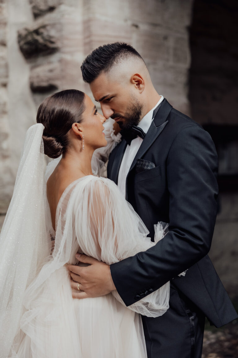 Braut und Bräutigam in Hochzeitskleidung umarmen sich draußen eng und blicken sich liebevoll in die Augen.